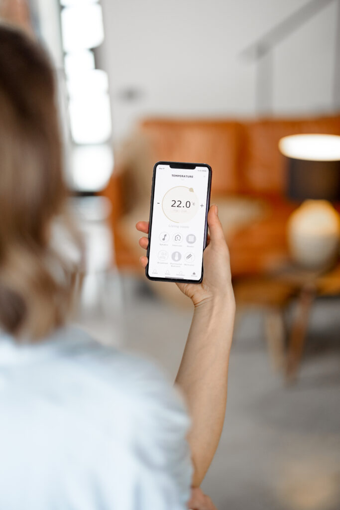 Woman with Smartphone with launched application for air temperature adjustment, air quality monitoring. Health microclimate at home concept.