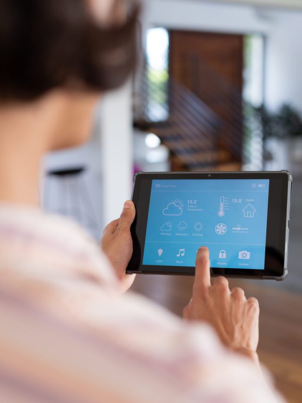 Vertical of hands of biracial man at home using tablet with smart home interface, copy space. Communication, technology and domestic life concept. Vertical of hands of biracial man at home using tablet with smart home interface, copy space. Communication, technology and domestic life concept.